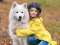 Dziewczynka w żółtej kurtce przytula puszystego samoyeda.